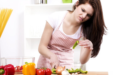 Obraz na płótnie Canvas ładna kobieta w kuchni, patrząc na kawałek zdegustowany paprykę