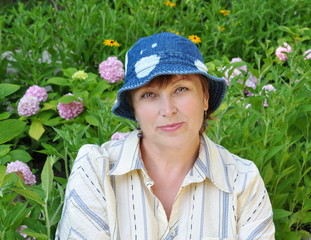 Senior woman in jeans panama sitting in her garden
