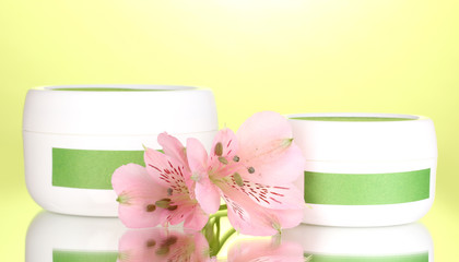 Jars of cream with flower on green background