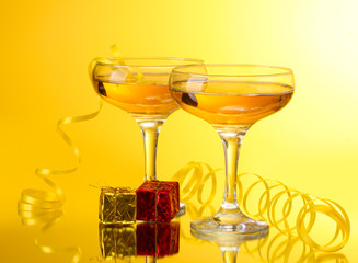 glasses of champagne, gifts and streamer on yellow background