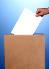 Hand with voting ballot and box on blue background