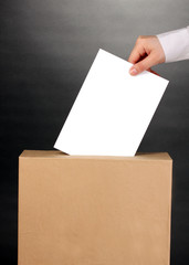 Hand with voting ballot and box on grey background