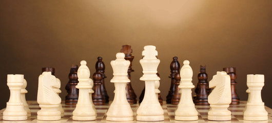 Chess board with chess pieces on brown background