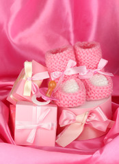 pink baby boots, pacifier, gifts on silk background.