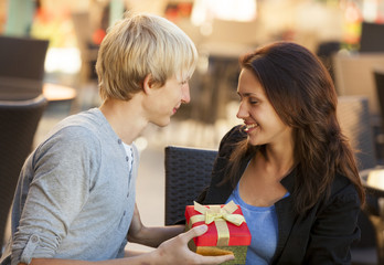 The young man gives a gift to a young girl in the cafe