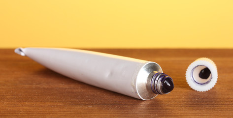 Tube with blue watercolor on wooden table on bright background