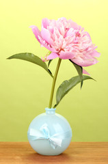 Pink peony in vase on wooden table on green background