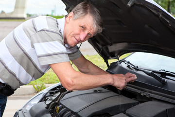 Mature man checking a oil level under car engine jacket