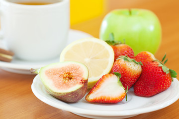 cup of tea,cookie,apple, lemon, fig and strawberries on a plate