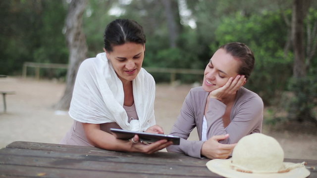 Two happy women with tablet computer in the park