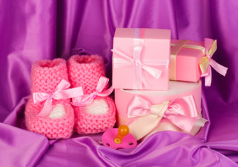 pink baby boots, pacifier, gifts on silk background.