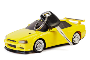 Fototapeta premium Car key lays on the yellow toy car, isolated on white