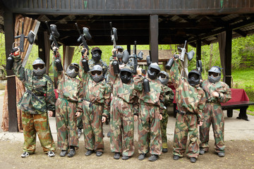 Boys dressed in camouflage stand in a row on a paintball base - obrazy, fototapety, plakaty