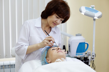 Beautician in beauty salon makes eyebrow tattooing for woman.