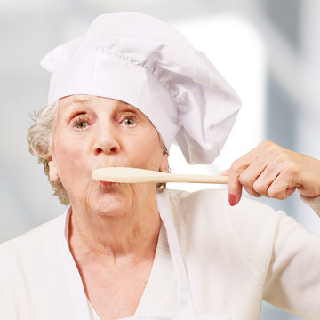 portrait of cook senior woman with wooden spoon on mouth indoor