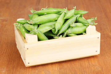 Green peas in crate on wooden background