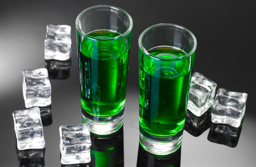 Two glasses of absinthe and ice on grey background