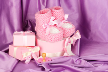 pink baby boots, pacifier, gifts on silk background.