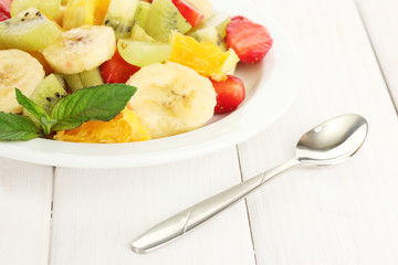 Fresh fruits salad on plate on white wooden table