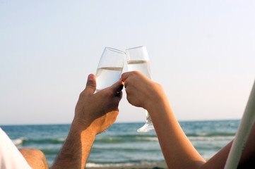 Two hands holding glasses at the beach