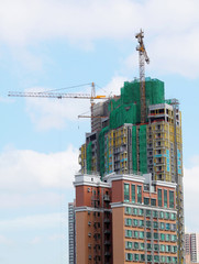 Naklejka premium Building crane and building under construction against blue sky
