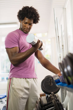 Young Black Man Taking Weights From Rack In Gym