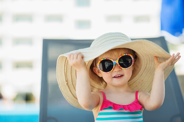 Portrait of baby in hat and glasses sitting on sun bed