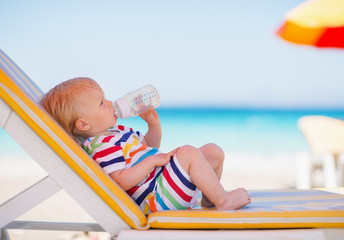 Portrait of baby on sunbed drinking water - obrazy, fototapety, plakaty