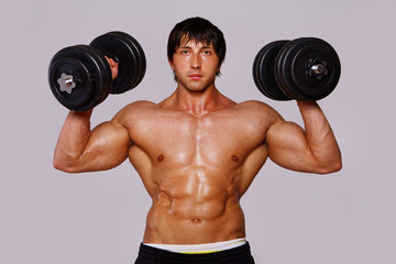 Fototapeta na wymiar Portrait of muscle man on grey background with dumbbels