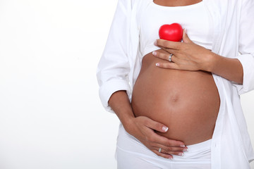 pregnant woman holding a heart above her exposed tummy