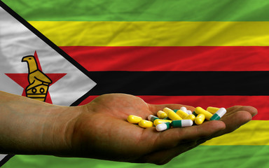holding pills in hand in front of zimbabwe national flag
