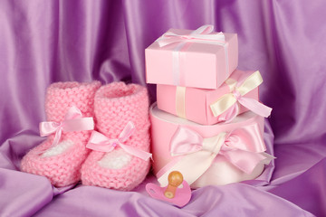 pink baby boots, pacifier, gifts on silk background.