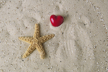 Ein rotes Herz oberhalb eines Seesterns auf feinem Sand