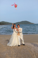 groom and bride standing with bouquet flowers at sea side