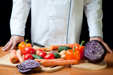 Chef standing by the kitchen table with variety of vegetables