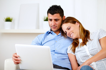 Lovely couple smiling and reading on laptop
