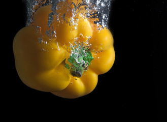 Yellow paprika and water splash on a black background.