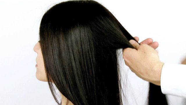 Hairdresser ironing long brunette hair of female model