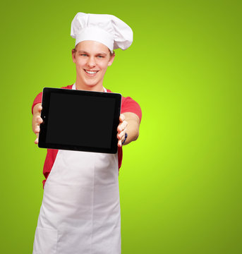portrait of young cook man showing a digital tablet over green b
