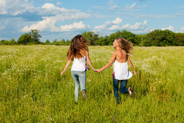 Two happy young women running on green field under blue sky