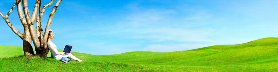 Pretty woman sitting with laptop under tree. Beautiful panoramic