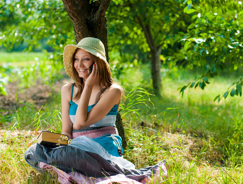Young beautiful woman holding book and speking on mobile in park