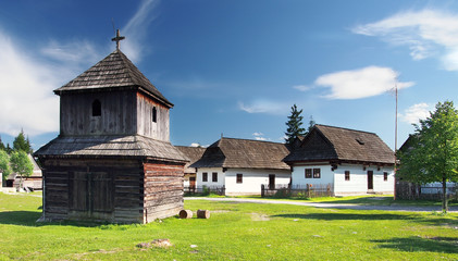 Rare wooden bell tower with folk houses in background.