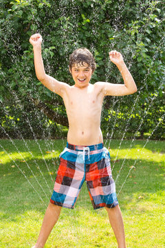 Endlich Sommer - Junge steht im Wasserstrahl, Rasensprenger