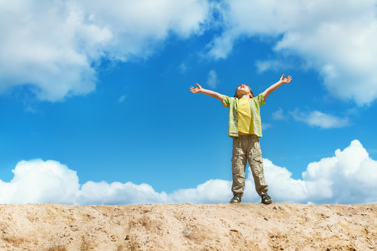 Happy child standing with hands raised up over sky on the top