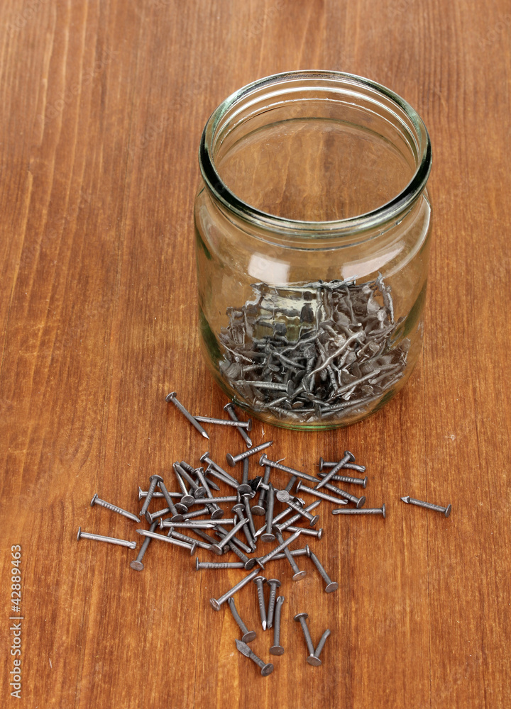 Wall mural metal nails and glass jar on wooden background