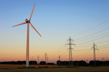 Wind turbine and electricity pylons against sky at sunset