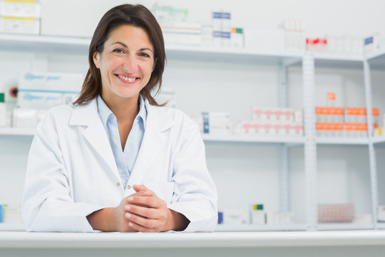 Smiling woman pharmacist behind a counter joining her hands