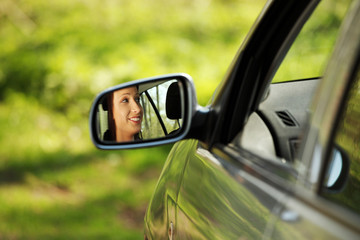 Face of women driving the car which is visible in mirror.