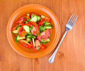 Fresh salad with tomatoes and cucumbers on wooden background